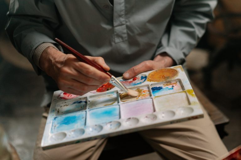 Artist mixing paint on a palette showcasing types of art medium.