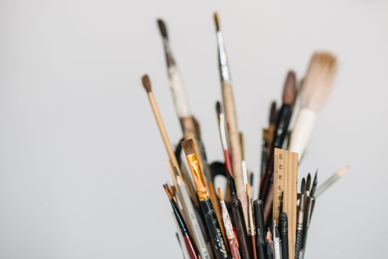 A close-up of a container holding a variety of tools for beginner artists, including paint brushes, pencils, and a ruler.