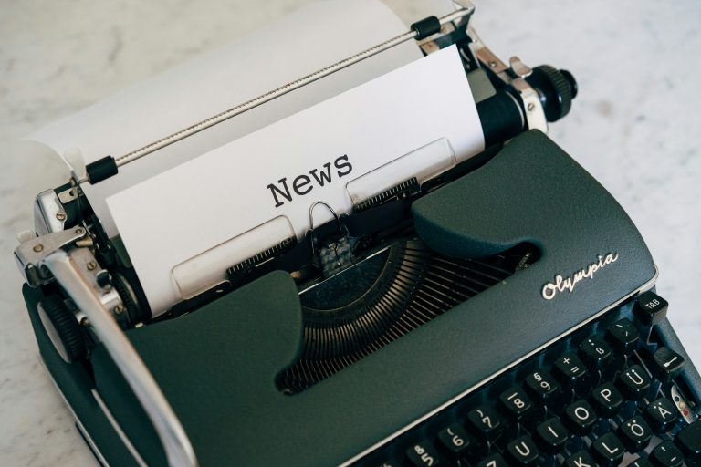 Vintage dark green Olympia typewriter with the word News typed on paper, representing the basics of journalism.